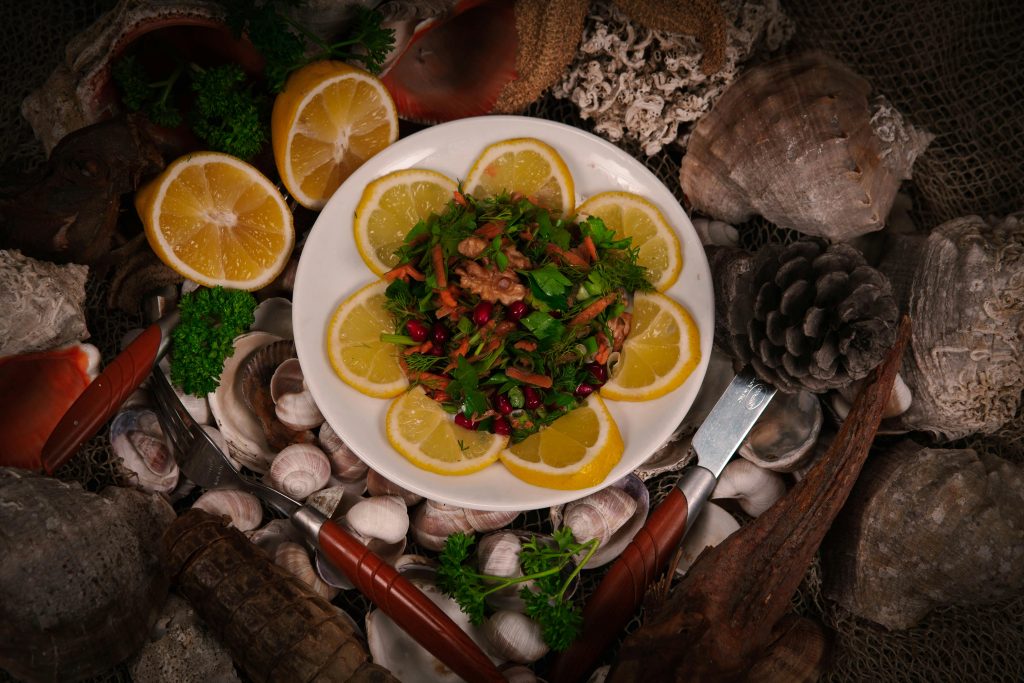 Colorful salad with lemon slices and nuts on a plate, surrounded by seashells and pine cones, creating a natural aesthetic.