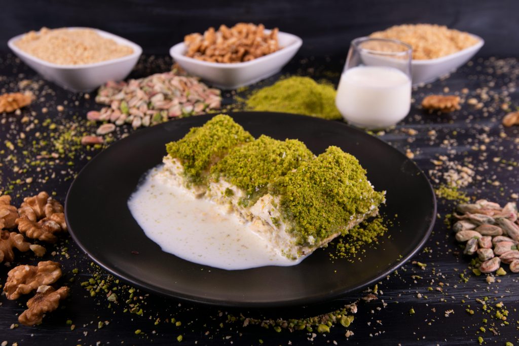 Close-up of a creamy Turkish dessert topped with pistachios, served with milk and nuts.